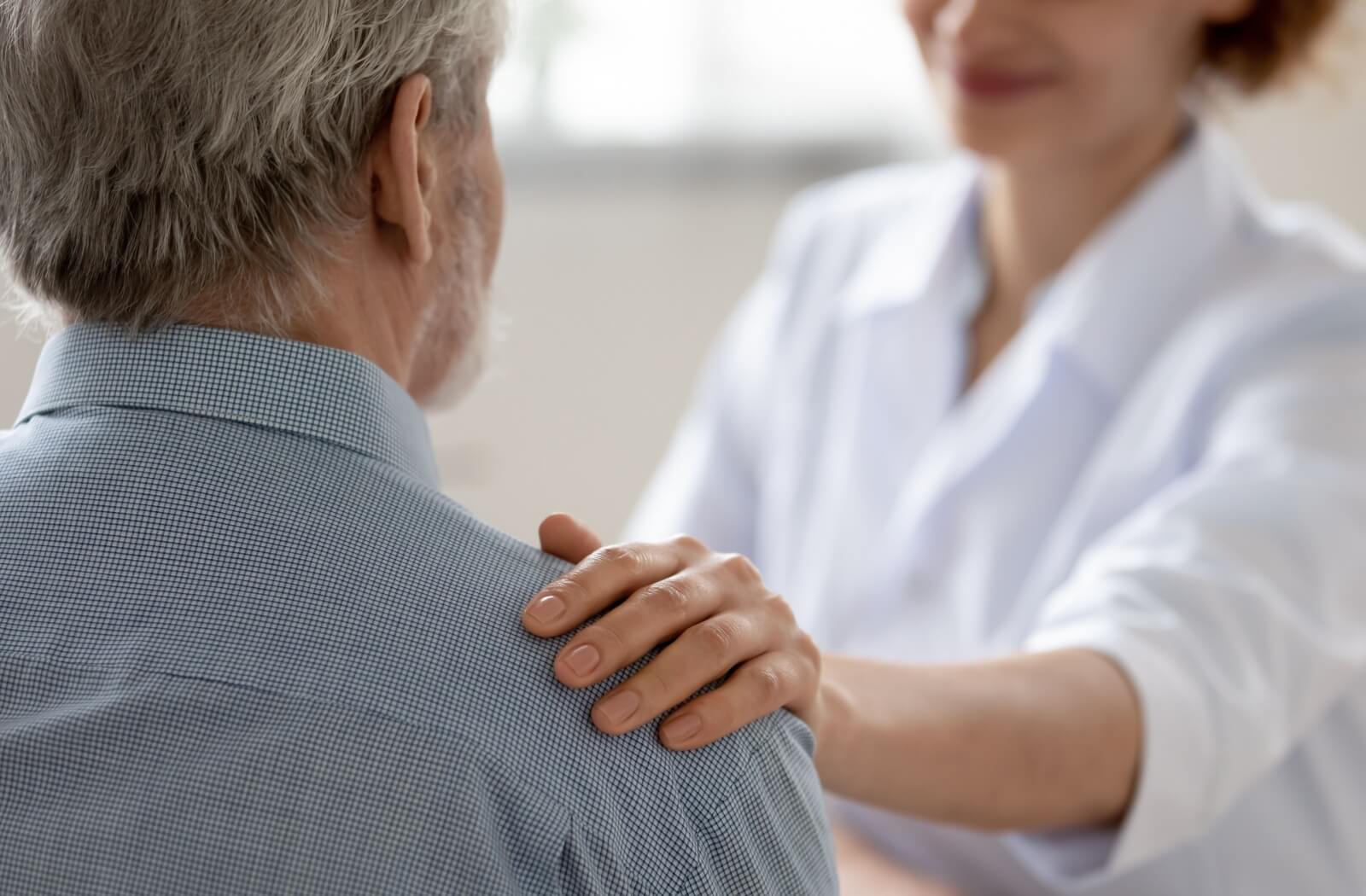 a caregiver putting their hand to a shoulder of a senior person with dementia for support